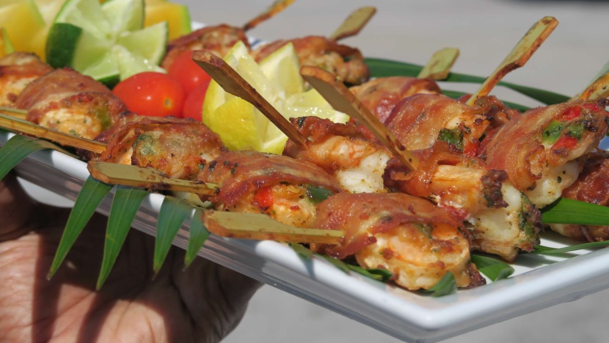 Shrimp Calyspo Platter of skewered shrimp wrapped in bacon, garnished with lime and tomatoes.