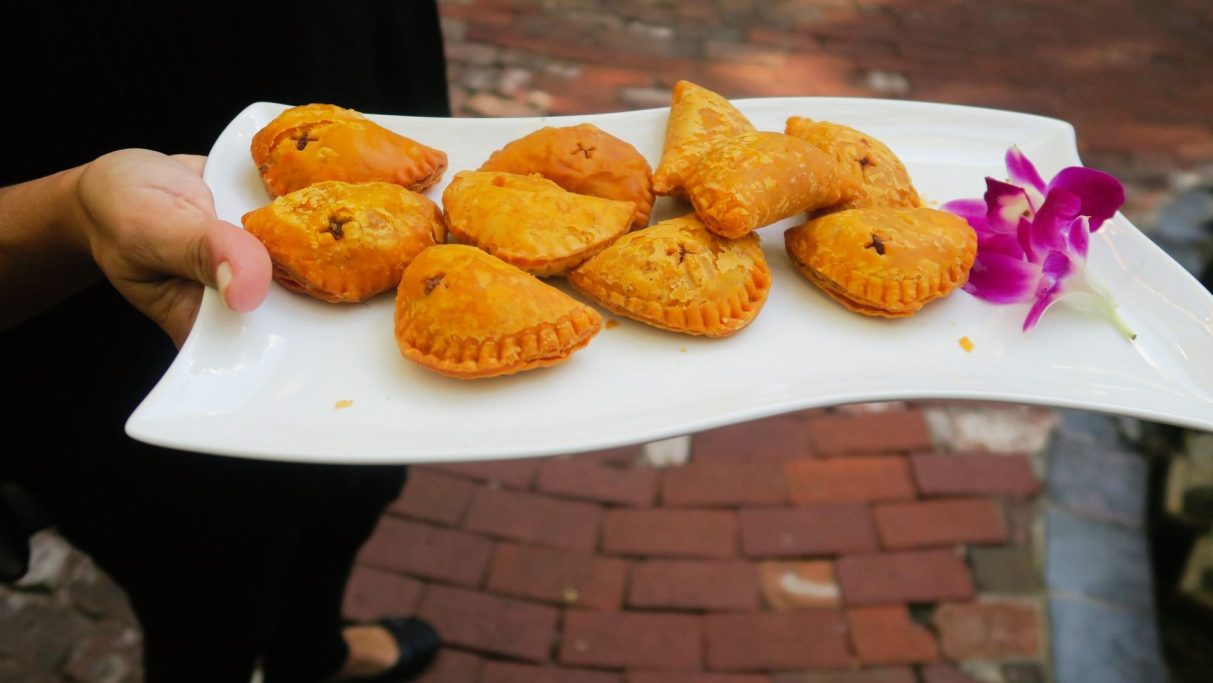 Mini Beef Empanada A plate of golden-brown pastries with a purple flower garnish.