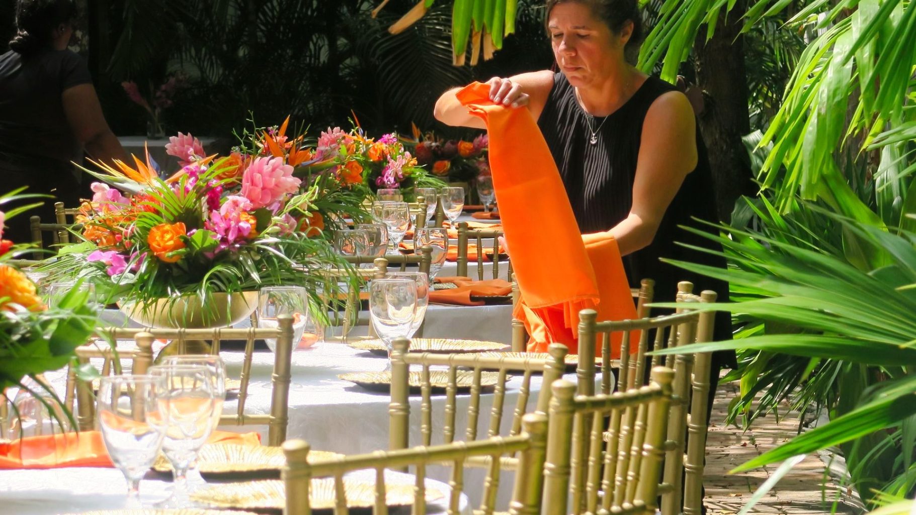 Crew Team A person arranges an orange napkin on a beautifully set outdoor dining table.