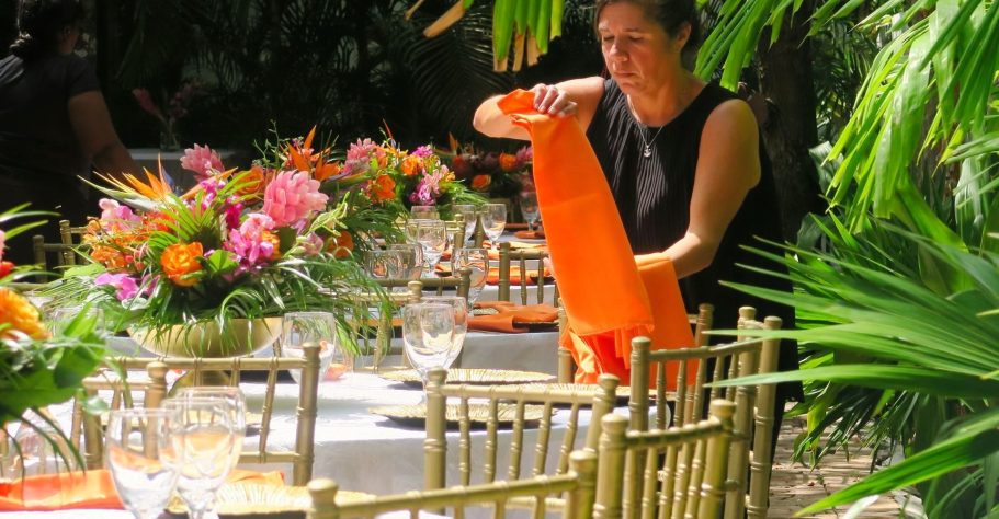 Destination Catering staff arranging orange table linens at a floral-decorated dining setup.