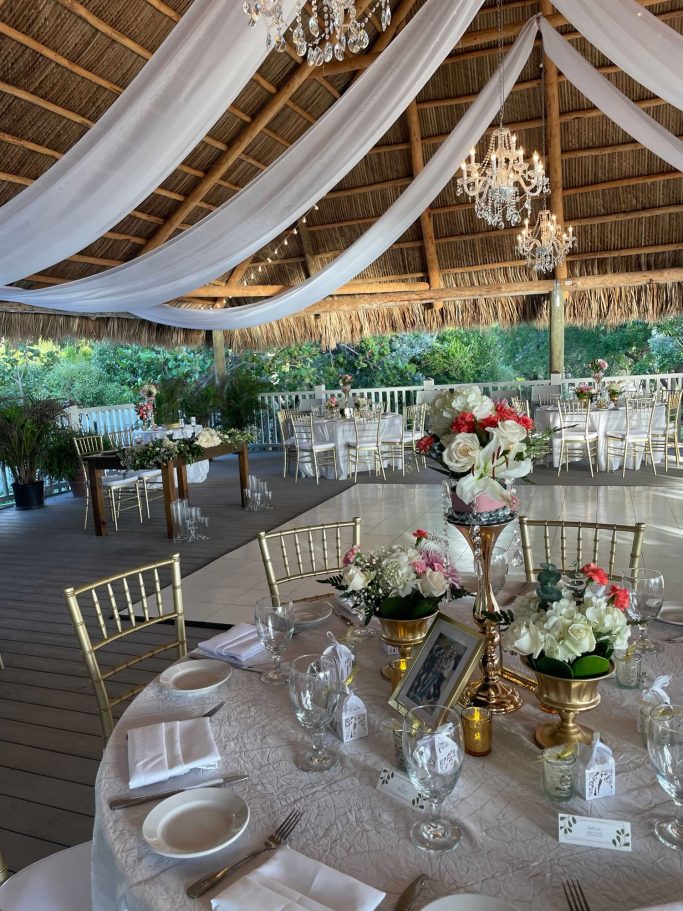 Tiki Hut Elegant wedding reception setting with tables, floral centerpieces, and draped fabric.