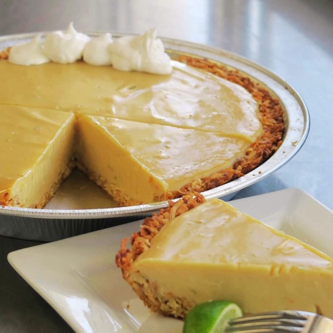 Key lime pie with whipped cream, one slice removed and served on a plate.