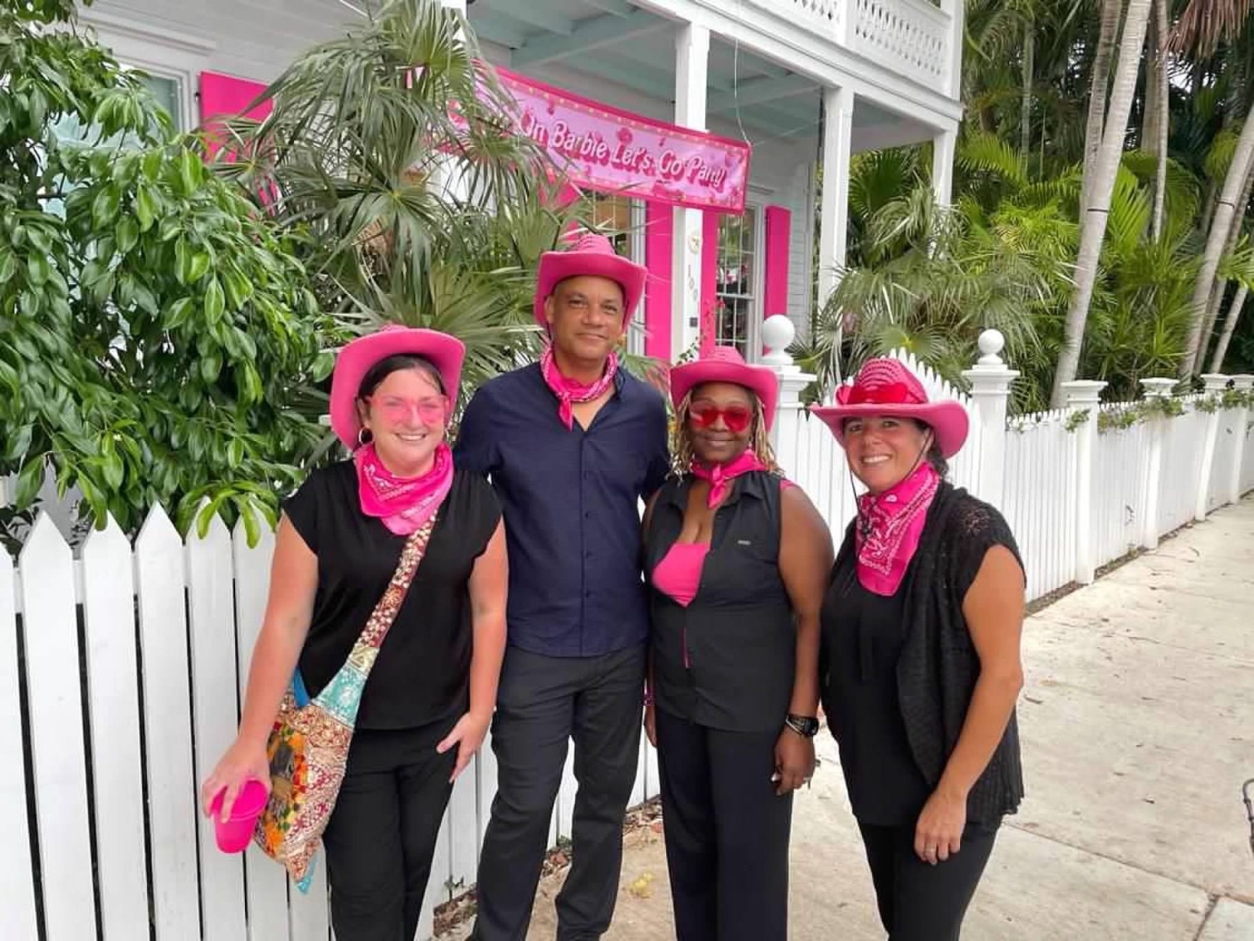 Team Members Four people in pink hats and scarves pose outside a pink-themed building.