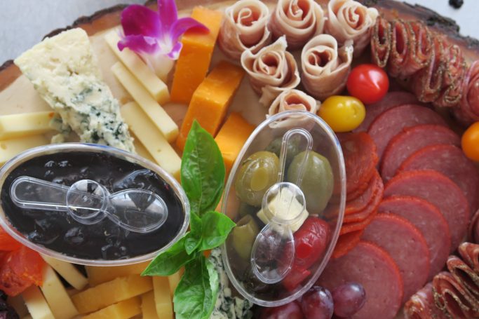 Corporate Catering A gourmet cheese and charcuterie board with assorted meats, cheeses, olives, and a flower garnish.
