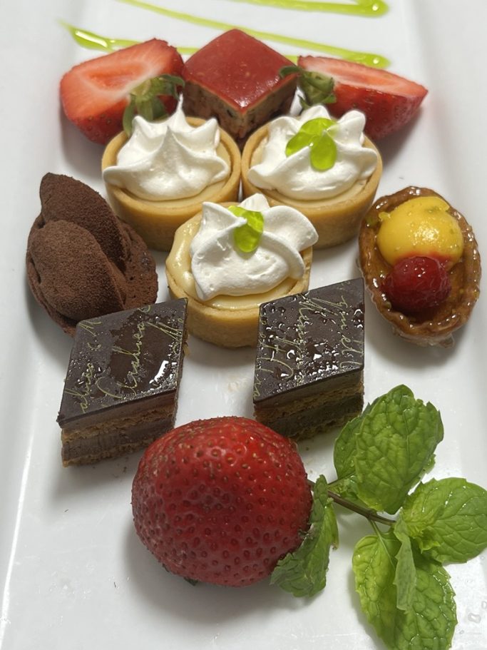 A colorful dessert platter featuring tarts, strawberries, mint, and chocolate pieces.