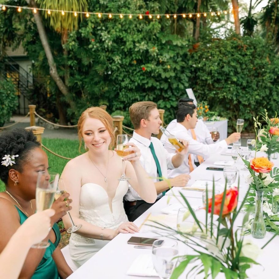 A joyful wedding celebration with guests toasting at a beautifully decorated outdoor table.