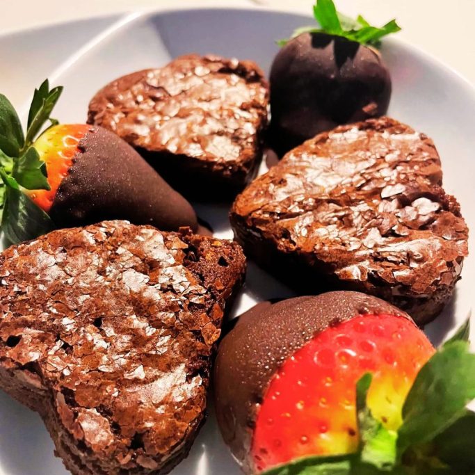 Heart-shaped brownies with chocolate-covered strawberries on a white plate.