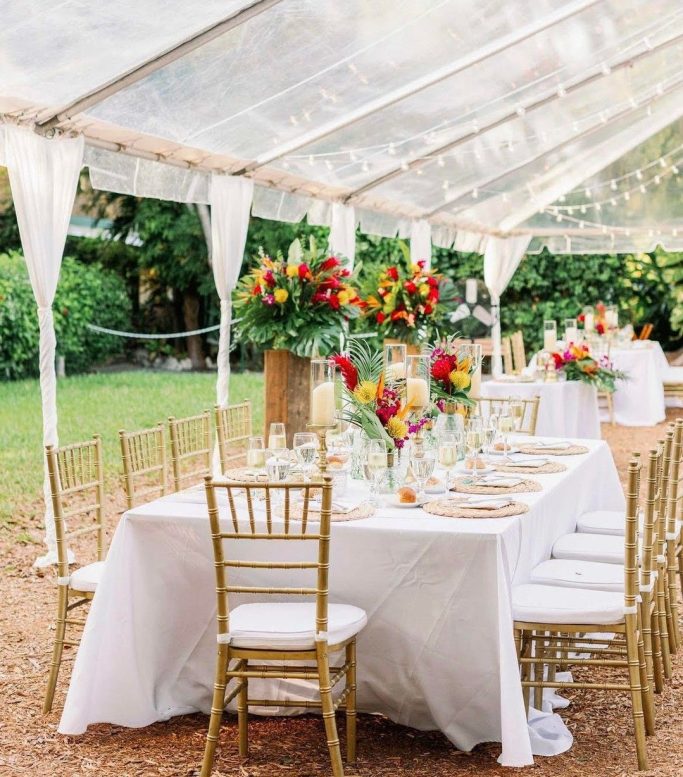 Florida Keys Wedding Vibe. Elegant outdoor dining setup under a tent with floral centerpieces and gold chairs.