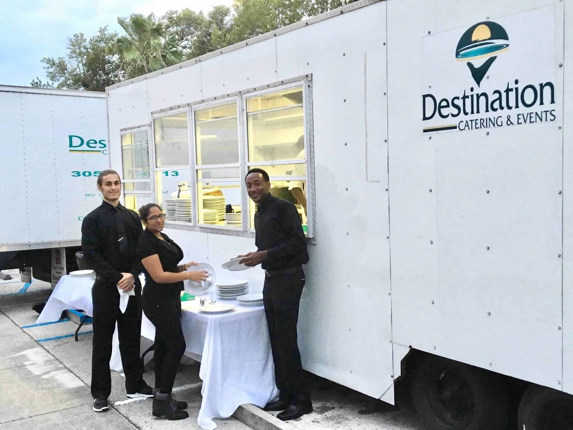 Catering Team Members Three staff members in black attire at a catering service trailer.