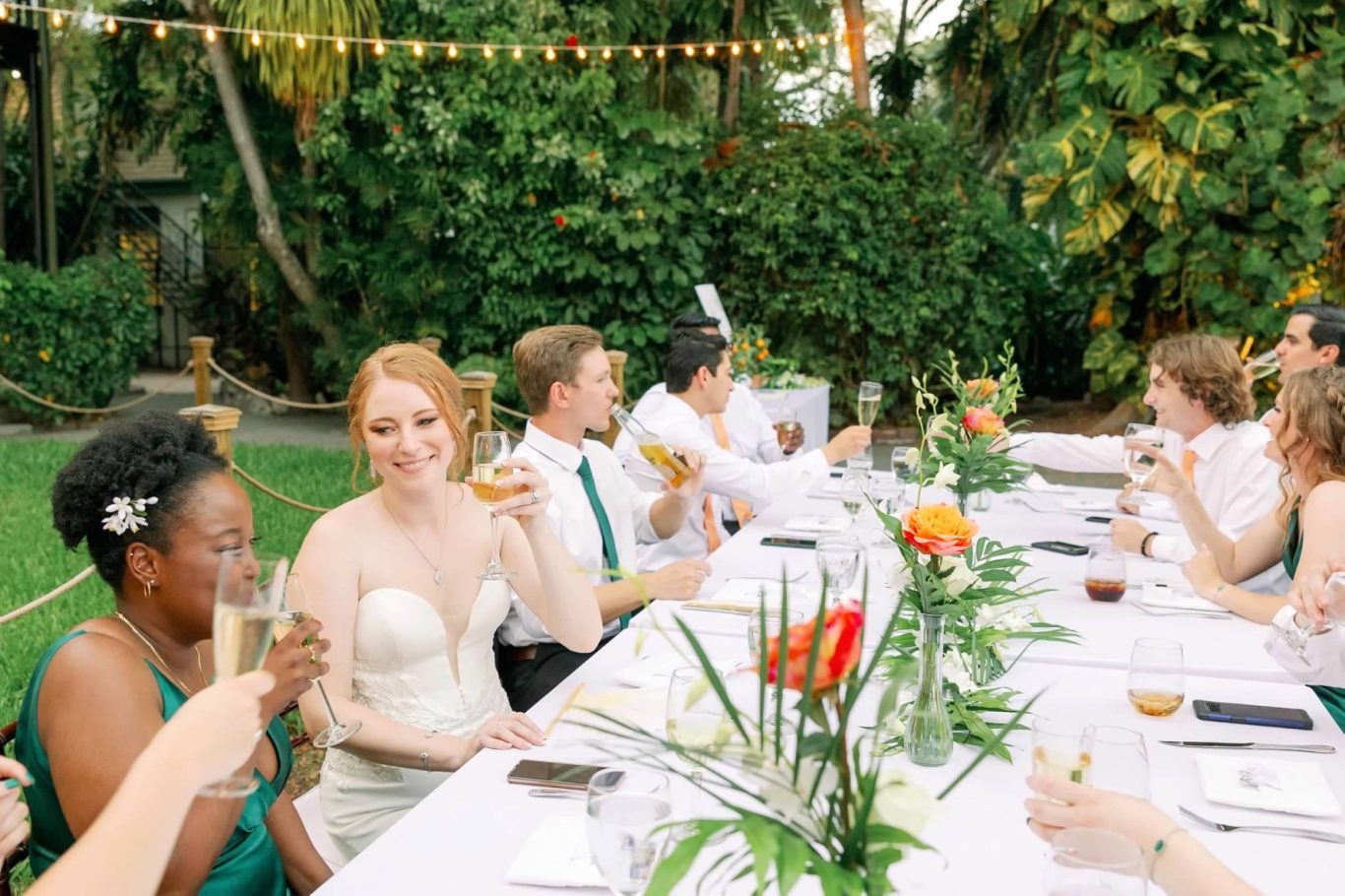 Toast to the Wedding Party A wedding reception with guests toasting at a long table decorated with flowers.